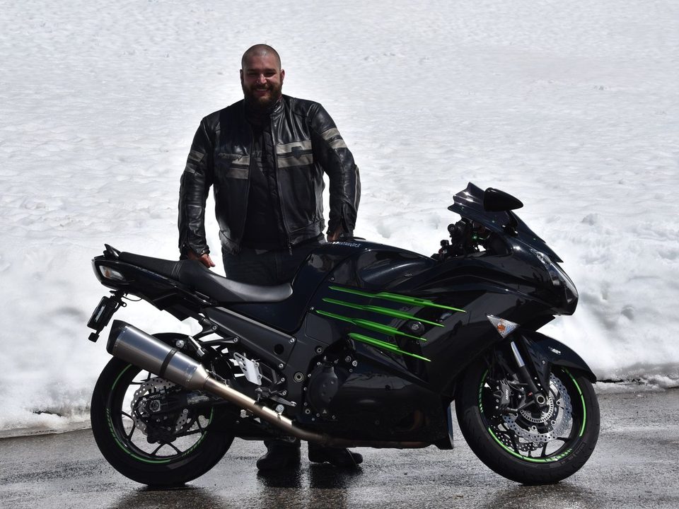 Steffen Broszeit neben seinem Motorrad auf einer Passstrasse mit Schnee